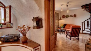 Una sala de estar acogedora, con suelo de madera, un sofá, una silla, una mesa con un jarrón de flores y una lámpara de pared.