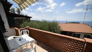 Ein Balkon mit Tisch und Stühlen, Blick auf das Meer und einem Gitterzaun.