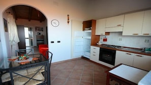 Une cuisine compacte avec des meubles blancs, une cuisinière et un réfrigérateur. On y trouve également un coin repas avec une table et des chaises.