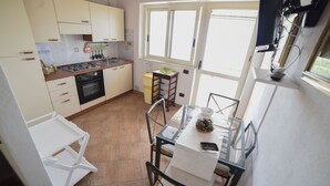 Eine kleine Küche mit Gasherd, Backofen und weißen Schränken. Ein Esstisch mit Stühlen und ein Fenster sorgen für natürliches Licht.