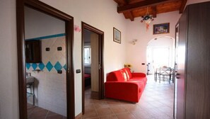 Un salon avec un canapé rouge, un coin repas avec une table et des chaises, et une cuisine visible à travers une porte ouverte.