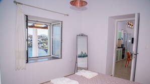 A bedroom with a bed, a window with a view, a mirror, and a door leading to a bathroom. - Sunrise Bay. Modern Cycladic House near the beach with a magnificent view. (Leros)