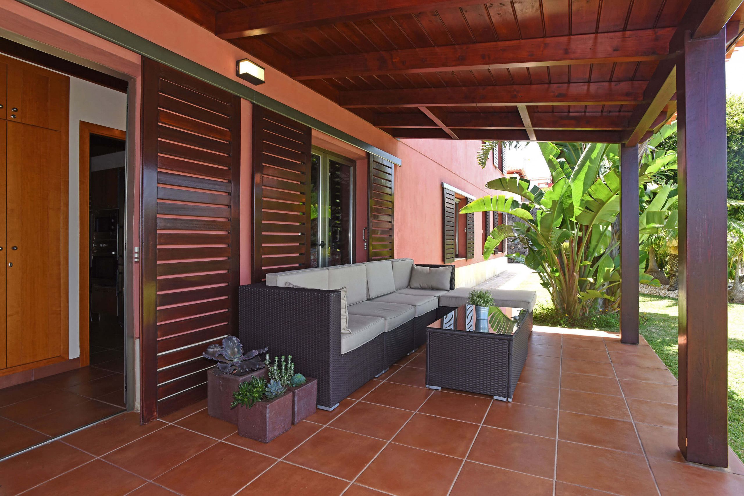 A covered patio with a sectional sofa, a small table, and potted plants.
