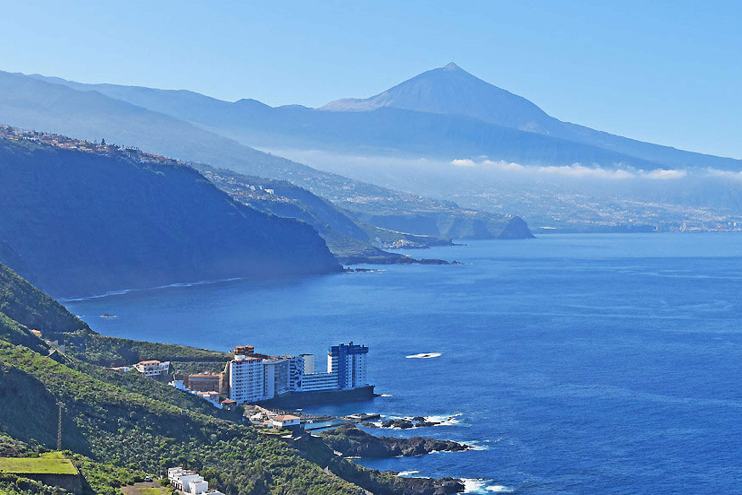 Ein Küstenhotel mit mehreren Gebäuden, Blick auf den Ozean und einem Berg im Hintergrund.