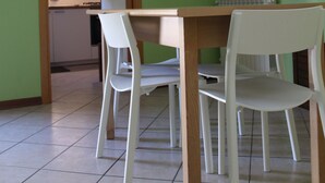 Un coin repas avec une table en bois et des chaises blanches, une cuisine en arrière-plan et des murs verts.