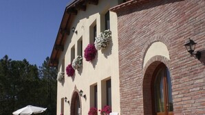 A building with a brick facade, multiple windows with flower boxes, outdoor seating, and a signboard. - POOL FARM - APARTMENT 4 PERSONS - 2 BEDROOMS 2 BATHROOMS  (La Serra)