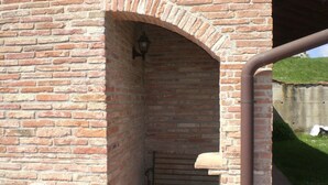 A brick archway leading to a covered outdoor area with a bench and a wall-mounted light fixture. - POOL FARM - APARTMENT 4 PERSONS - 2 BEDROOMS 2 BATHROOMS  (La Serra)