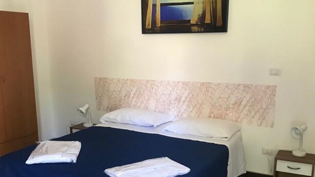 A neatly made bed with a blue bedspread and white pillows, a marble-patterned headboard, a painting of a landscape above the bed, and a wooden wardrobe to the left. - Holiday house in Palinuro center (Palinuro)