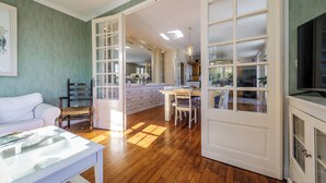 A spacious living room with a white sofa, a dining table, and a kitchen area visible through glass doors. - Rocaille, villa with private pool, views, privacy, comfort and service (Pujols)