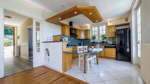 A modern kitchen with wooden cabinets, a black refrigerator, and a dining area with a white table and chairs. - Rocaille, villa with private pool, views, privacy, comfort and service (Pujols)