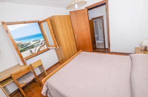 A bedroom with a large bed, a wooden desk, a chair, a window with a view of the sea, and a bathroom door. - Apartment Sea Breeze Deiva Marina 4 Tinetto (Deiva Marina)