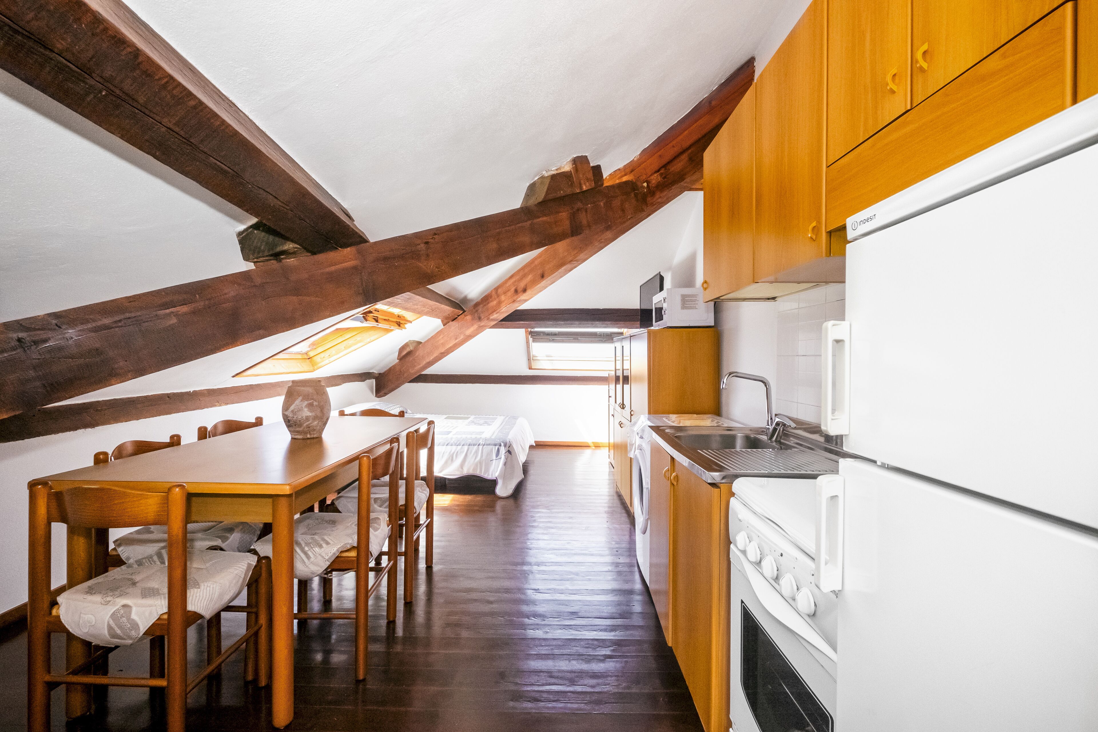 Eine kleine Küche mit Holzausbau, einem weißen Kühlschrank und einem Essbereich mit Tisch und Stühlen.