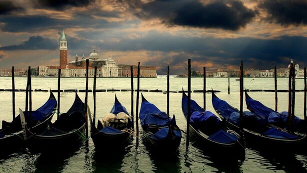 Gondolas amarradas en un muelle con un edificio histórico al fondo.