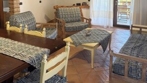 Um interior rústico com uma mesa de jantar de madeira, duas cadeiras estofadas, uma pequena mesa de madeira e um banco.