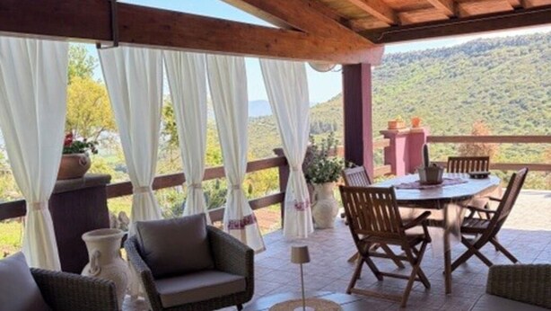 Um alpendre coberto com móveis de vime, uma mesa e vista para uma paisagem montanhosa.