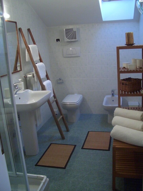 Une salle de bain équipée d’un lavabo, de toilettes, d’un bidet et d’une étagère avec des serviettes.