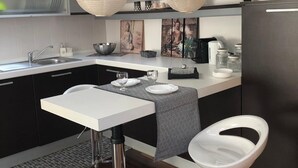Une cuisine moderne avec un coin repas, comprenant une table blanche, deux tabourets de bar, une nappe à motifs noir et blanc et des lanternes en papier suspendues.