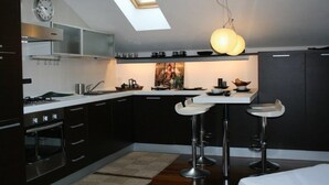 Une cuisine moderne dotée d’une verrière, de meubles de couleur sombre, d’un îlot central avec des tabourets et d’une horloge murale.