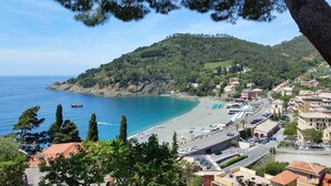 Une ville côtière avec une plage, une route bordée de voitures garées et des bâtiments aux toits recouverts de tuiles rouges.