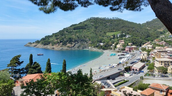 Uma cidade costeira com uma praia, uma estrada com carros estacionados e edifícios com telhados de telha vermelha.