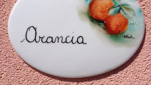 A white ceramic tile with the name "Orancia" and a watercolor painting of two oranges with leaves. - Lake Como - Residence La Collina - Orange (Vercana)