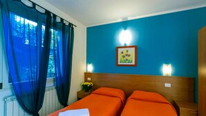 A hotel room with two beds, a blue wall, a framed picture, and a nightstand with a vase of flowers. - Lake Como - Residence La Collina - Orange (Vercana)