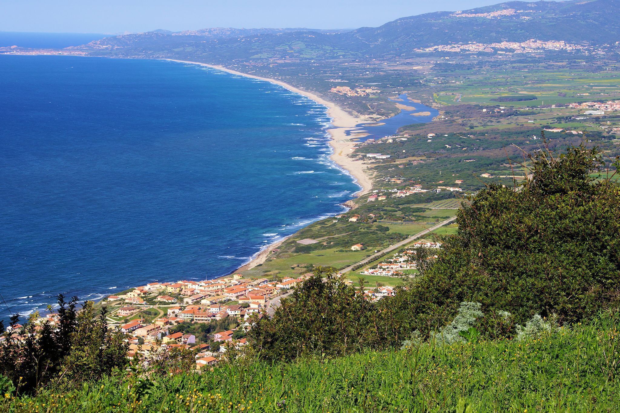 Un pueblo costero con playa, casas y zonas verdes.