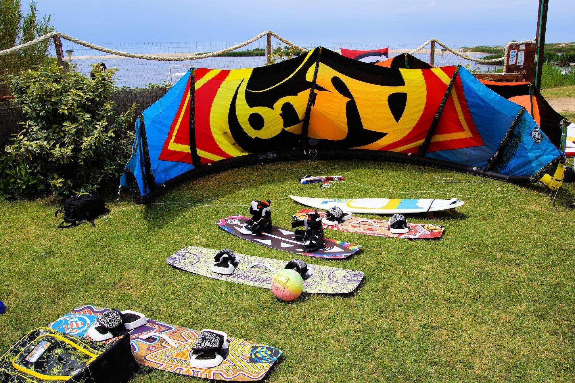 A grassy area with a large colorful tent, several surfboards, and a beach in the background.