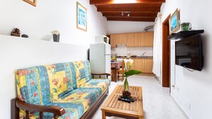A compact living space with a sofa, a wooden table, a kitchen area, and a TV mounted on the wall.