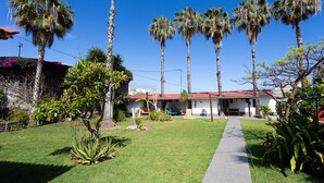 A house with a red-tiled roof, surrounded by a well-maintained lawn and tall palm trees.