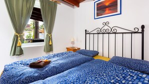 A bedroom with two beds, a window with green curtains, a painting on the wall, and a wooden ceiling.