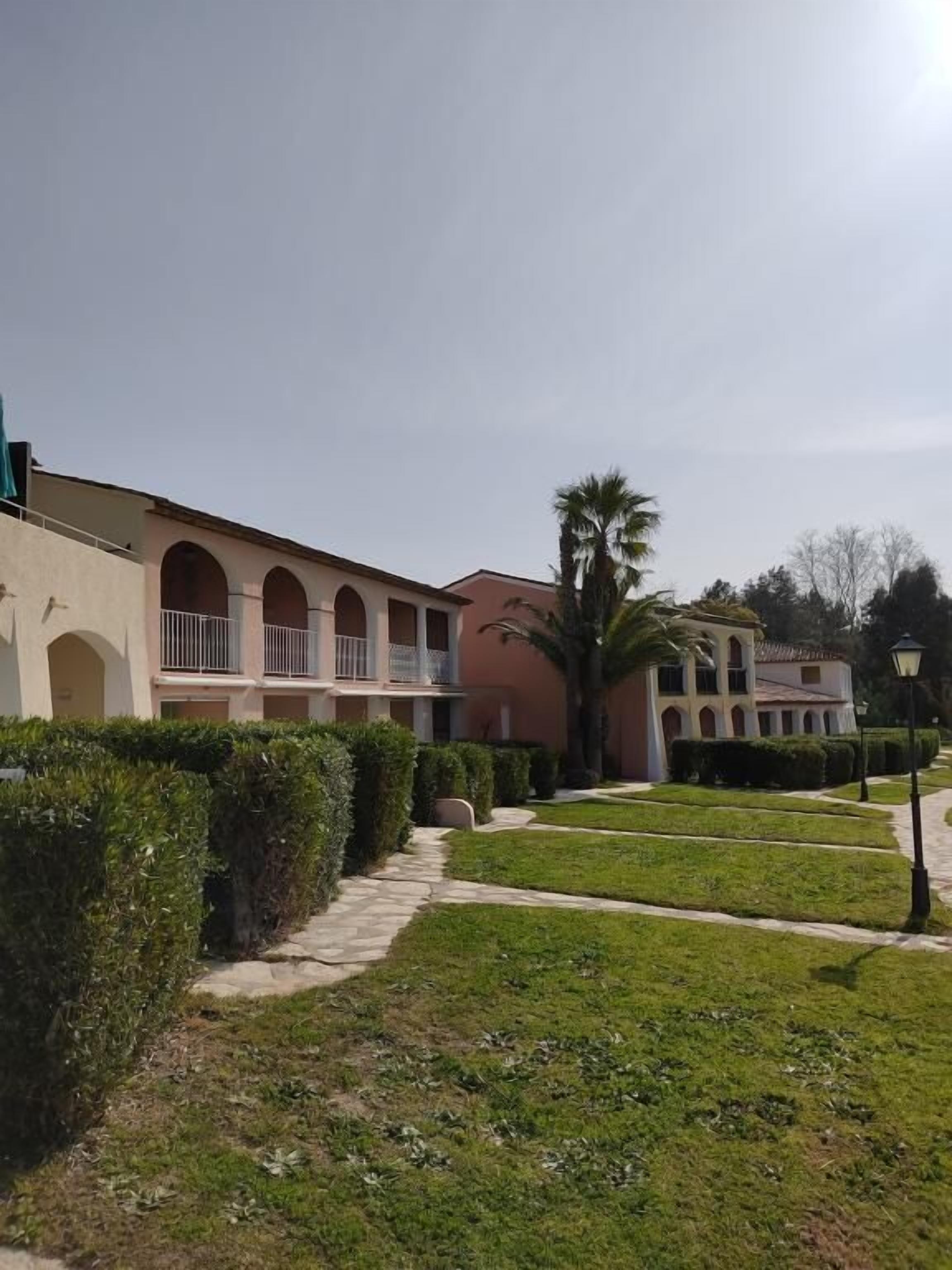 A building with multiple balconies and a well-maintained garden with hedges and a palm tree.