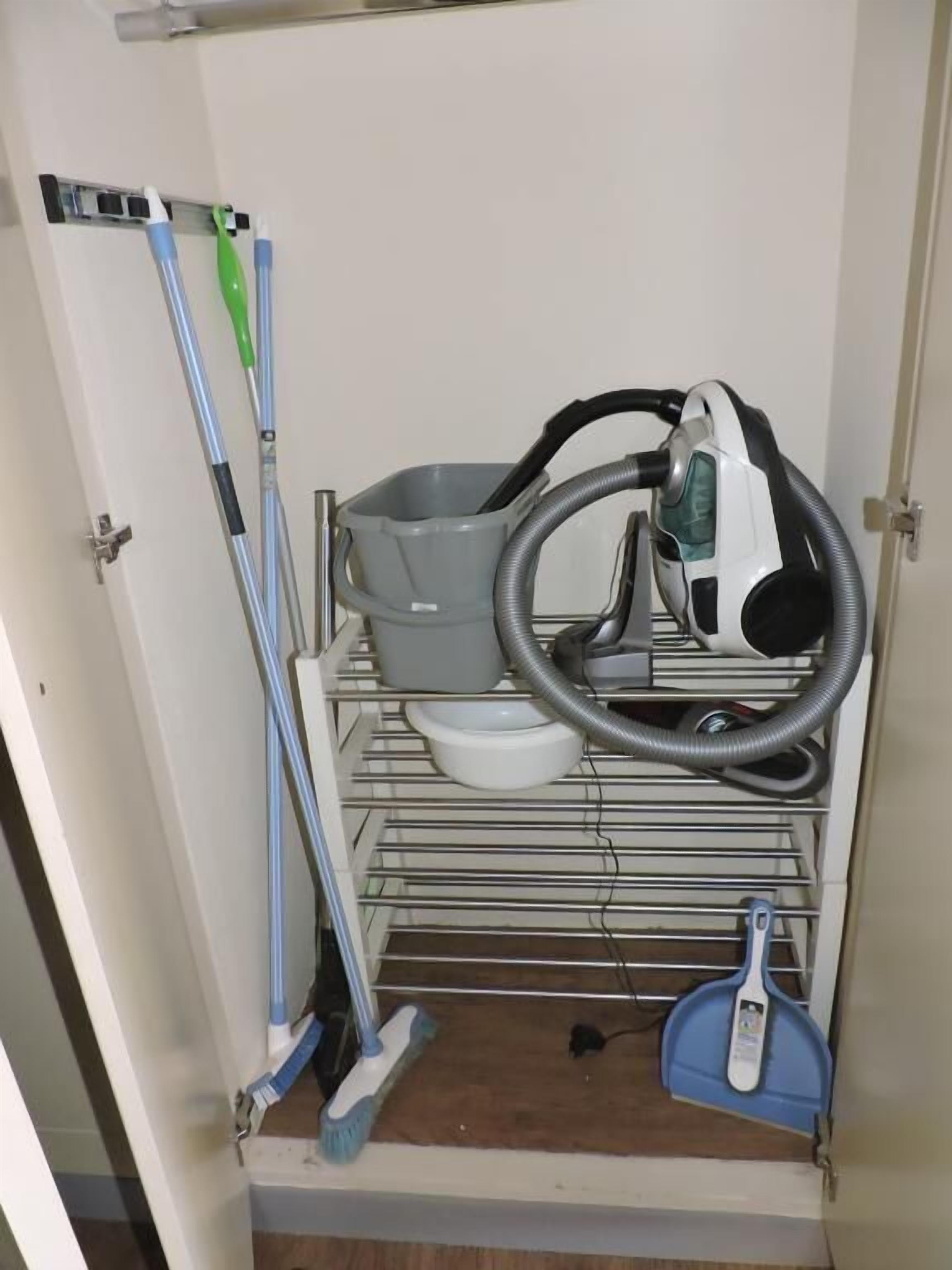 Un meuble de rangement compact doté d’étagères pour ranger les outils de nettoyage, un aspirateur et une serpillière.