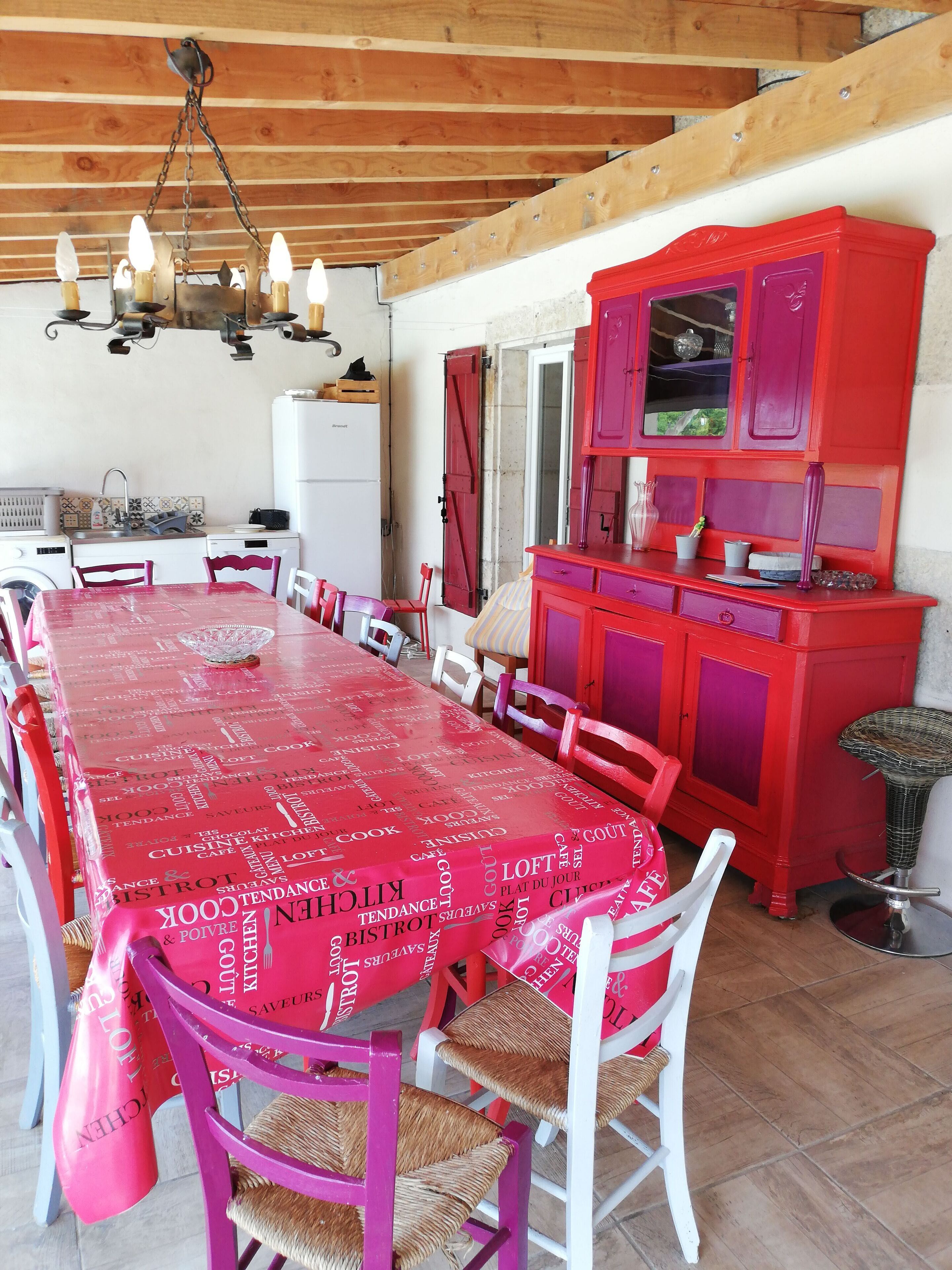 A dining area with a long table covered in a red tablecloth, surrounded by chairs.