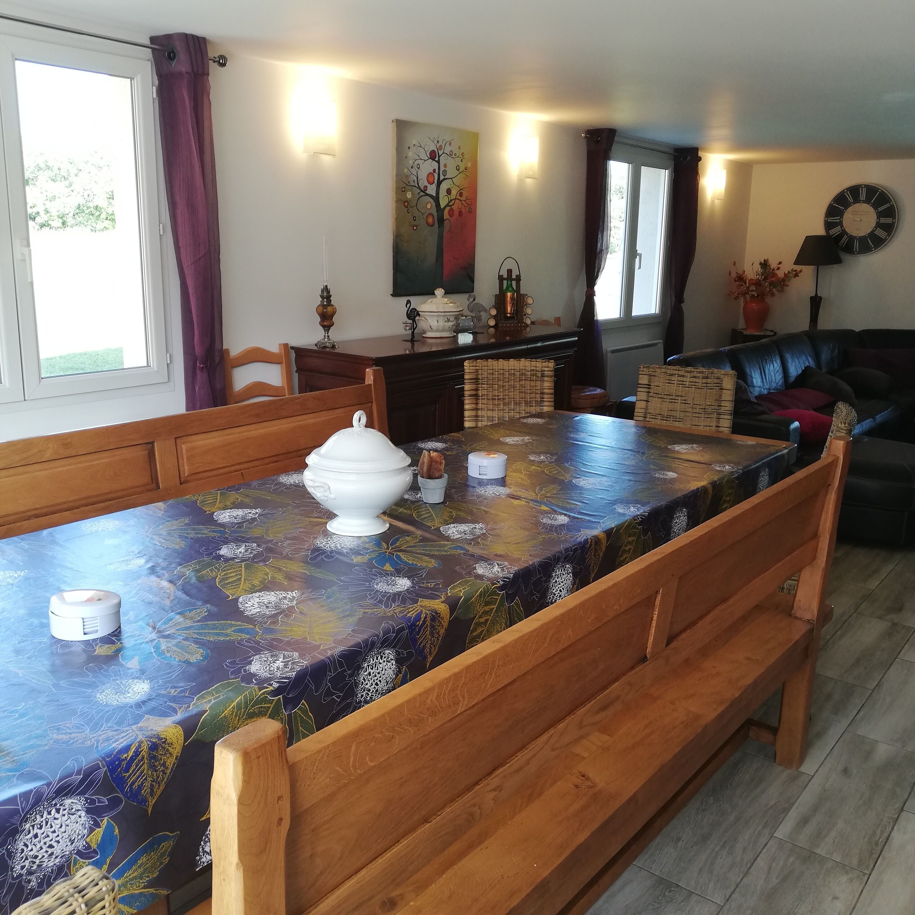 A dining area with a table set for four, a white tureen, and a vase with flowers.