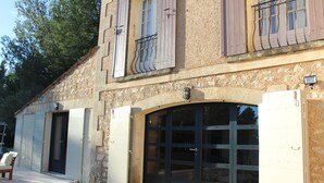 Un bâtiment en pierre doté d’un grand portail de garage, d’un petit balcon avec des balustrades en métal et d’une porte avec une poignée.