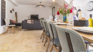Un espace de repas moderne avec une longue table dressée pour six personnes, un téléviseur en arrière-plan et un vase décoratif rempli de fleurs.