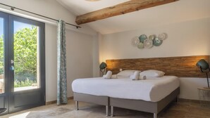 Une chambre moderne avec un grand lit, une poutre en bois au plafond, une porte en verre donnant sur un balcon et une lampe fixée au mur.