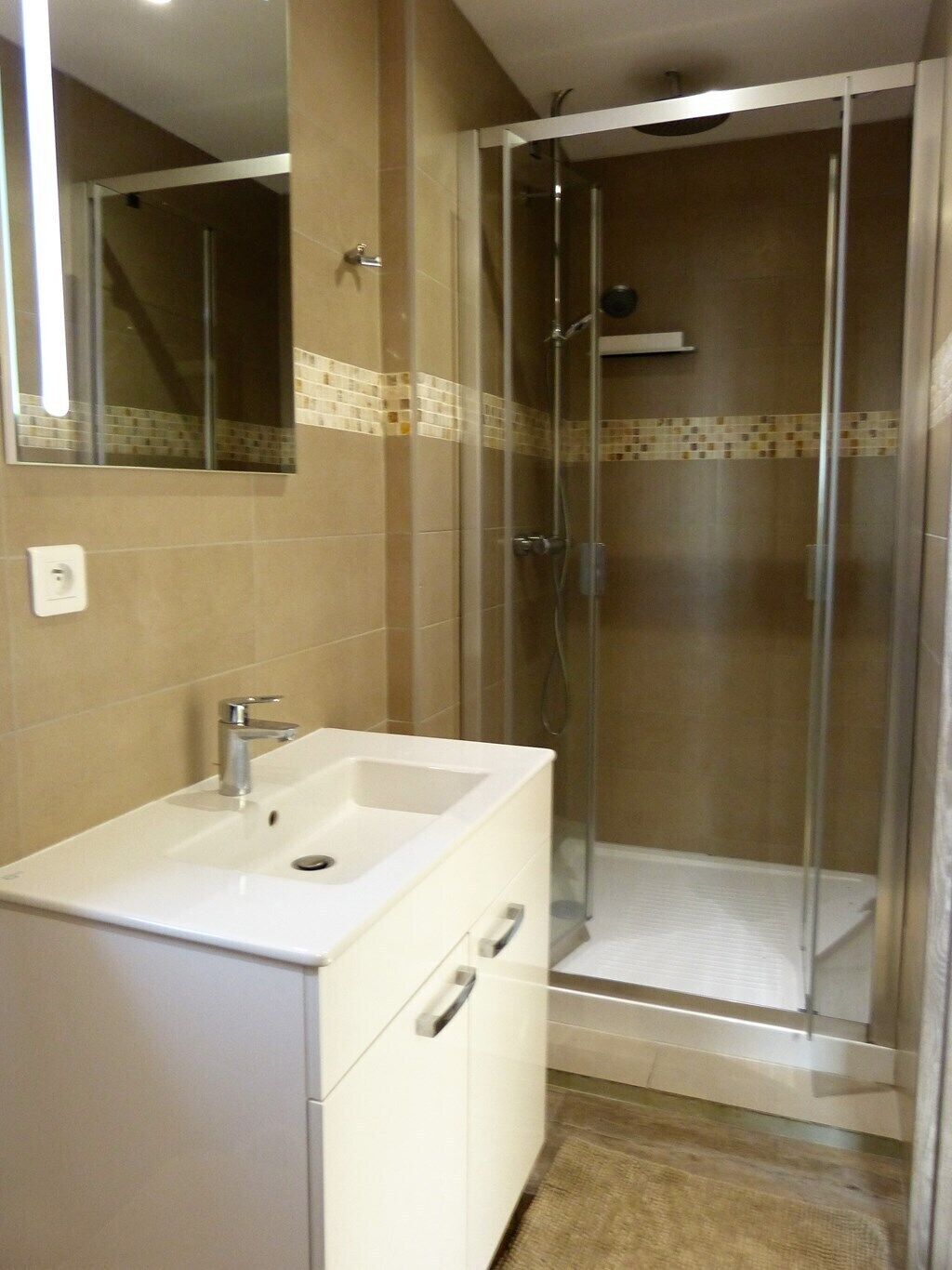 A bathroom with a white sink, a mirror, and a glass-enclosed shower.