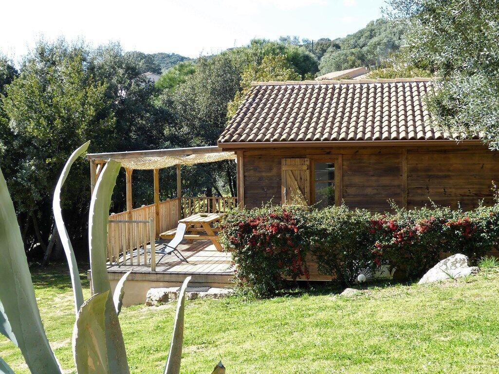 A wooden cabin with a tiled roof, a wooden deck, and a covered seating area.
