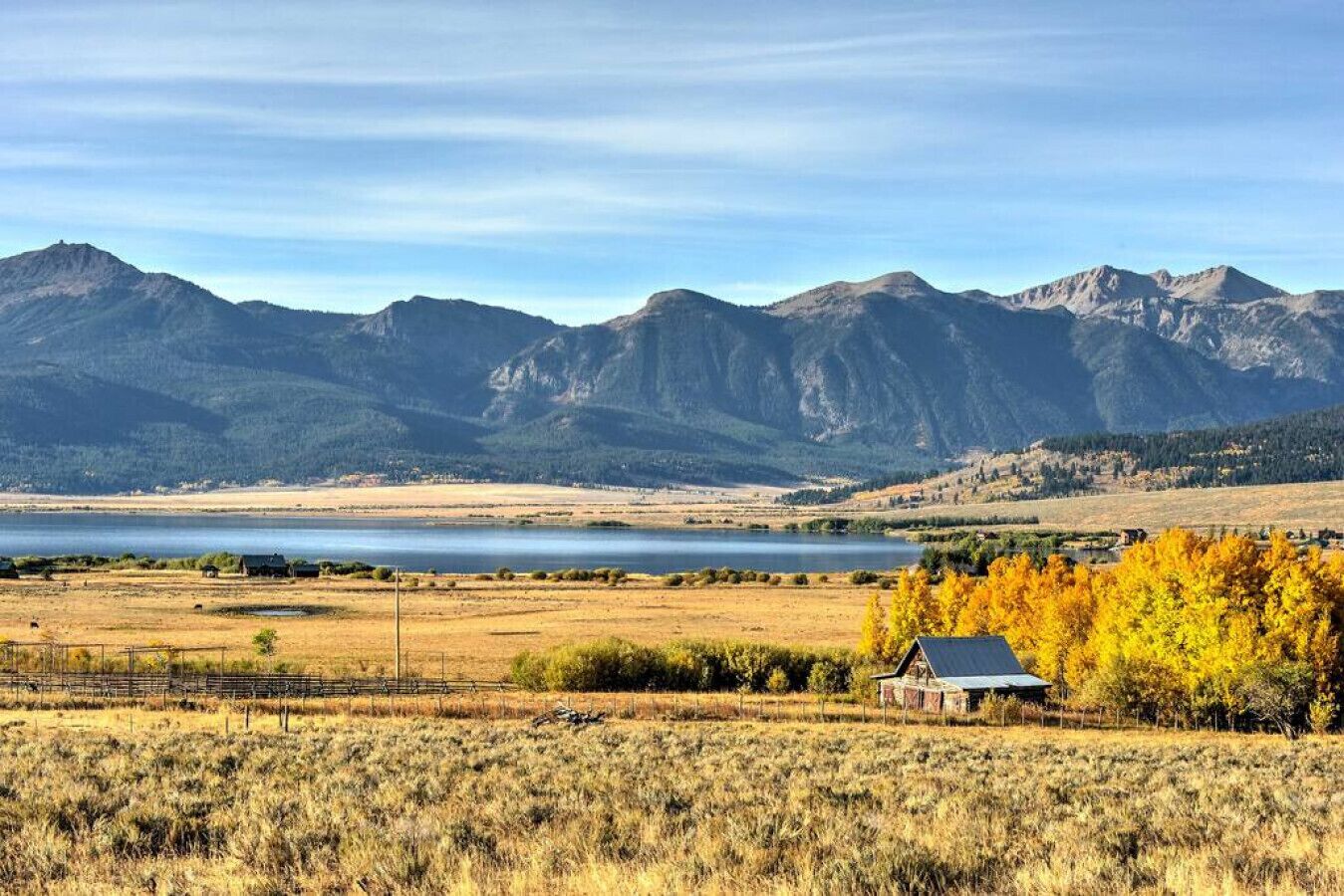 A rural landscape with mountains, a lake, and a small house in the foreground.