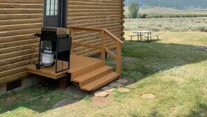 Una baita con veranda, una piccola cucina esterna e un tavolo da picnic in un prato erboso con montagne sullo sfondo.