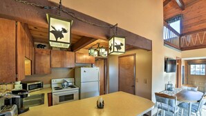 Una cucina con mobili in legno, un'isola centrale, un forno a microonde, un fornello, un frigorifero e lampade a tema alci.