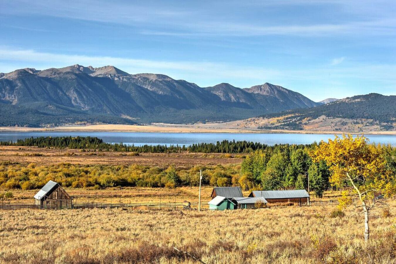 A rural landscape with mountains, a lake, and a few buildings.