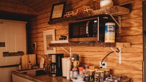 A kitchen with wooden walls, a microwave, coffee maker, and various jars and containers on the counter. - Glamping - UP NORTH - Riverside! (Fife Lake)
