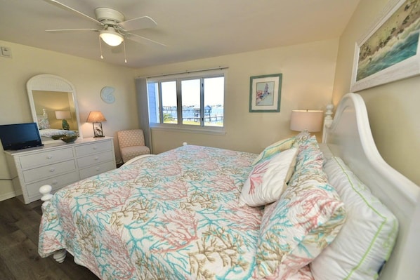 A bedroom with a bed, a desk, a chair, a window, and a ceiling fan.