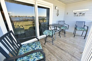 En balkon med udsigt over vandet, et bord og to stole med mønstrede hynder.