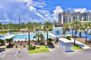 A hotel with a swimming pool, palm trees, and a parking lot.