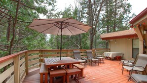 Une terrasse en bois avec une table de pique-nique, des chaises et un parasol.
