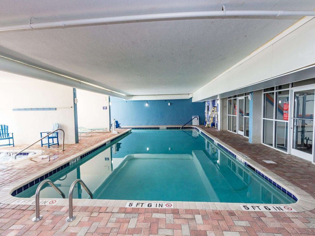 Une piscine intérieure avec un bord carrelé, un sol en briques et un plafond où les tuyaux sont apparents.